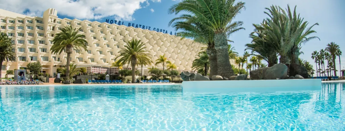 Vue sur la façade du bâtiment et la végétation tropicale qui entoure le bassin.