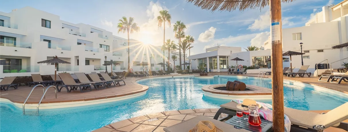 Une vue panoramique d'une grande piscine, bordée de transats et de bâtiments blancs modernes.