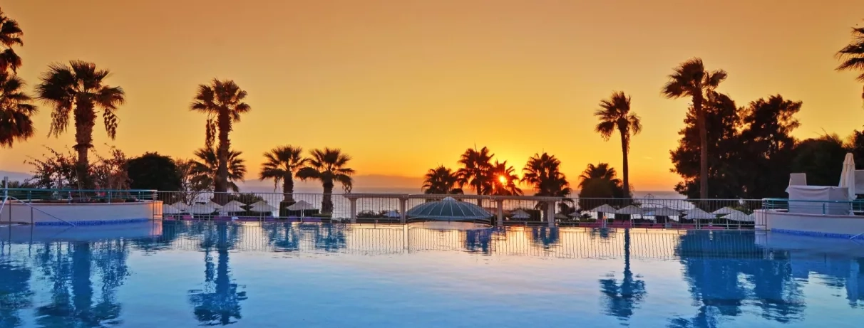 Un coucher de soleil flamboyant se reflétant sur l'eau de la piscine bordée de palmiers.