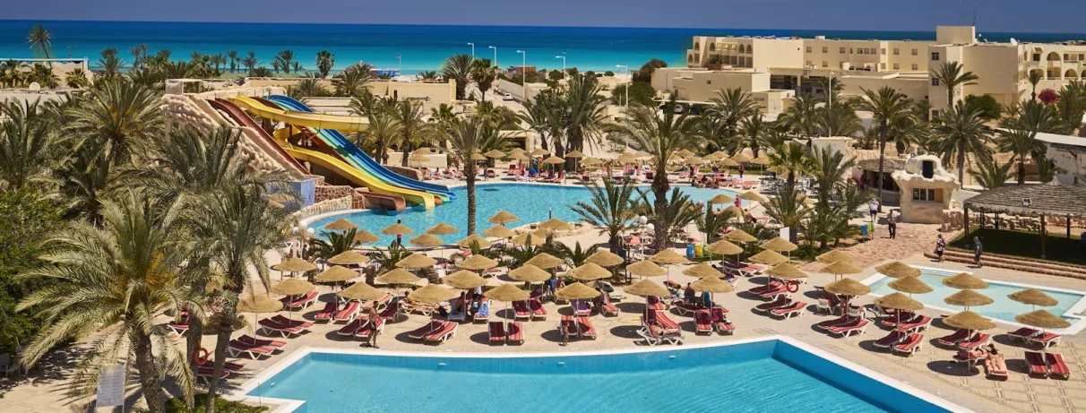 Parc aquatique avec toboggans colorés, piscines et palmiers au complexe hôtelier Quatre Saisons à Djerba, Tunisie.