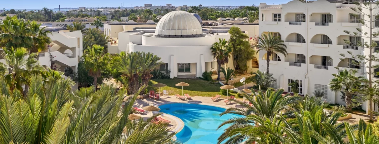 Architecture traditionnelle blanche et piscine turquoise entourée de palmiers dans l'hôtel Quatre Saisons à Djerba.