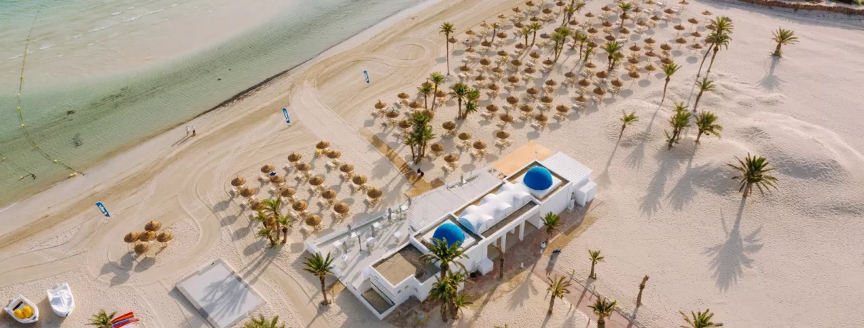 Plage aménagée avec transats et dômes bleus typiques face à la mer turquoise au Djerba Golf.