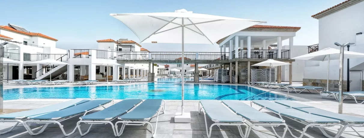Une vaste piscine ensoleillée bordée de transats confortables et d'un grand parasol blanc..