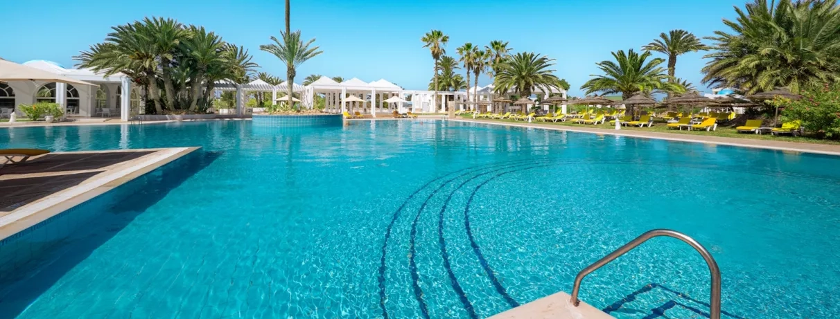 Grande piscine extérieure entourée de palmiers et de transats sous le soleil au Djerba Golf.
