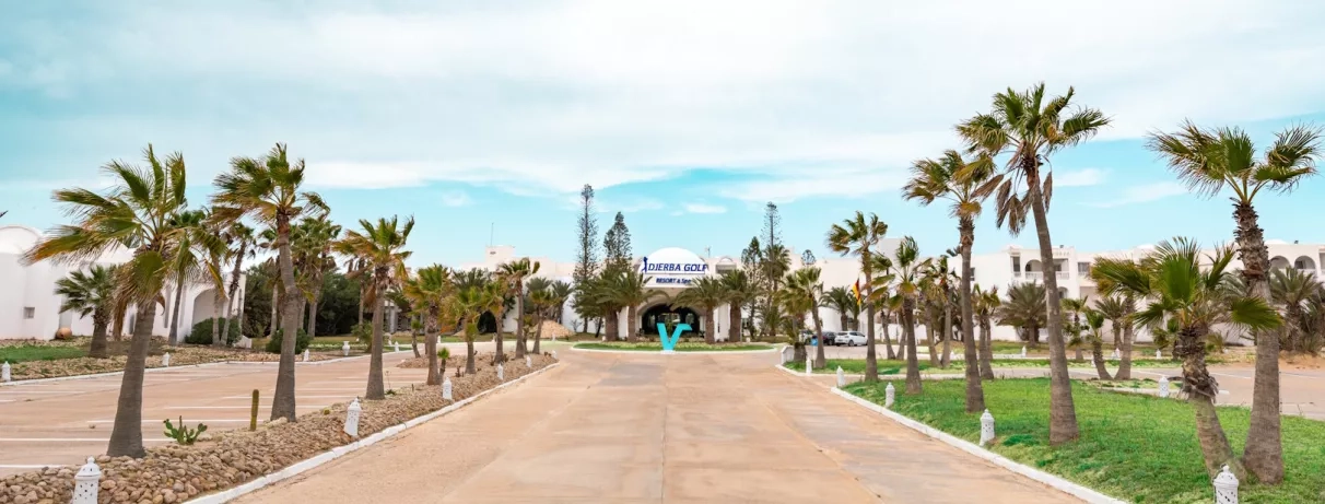 Entrée principale du Djerba Golf Resort & Spa bordée de palmiers sous un ciel azur.