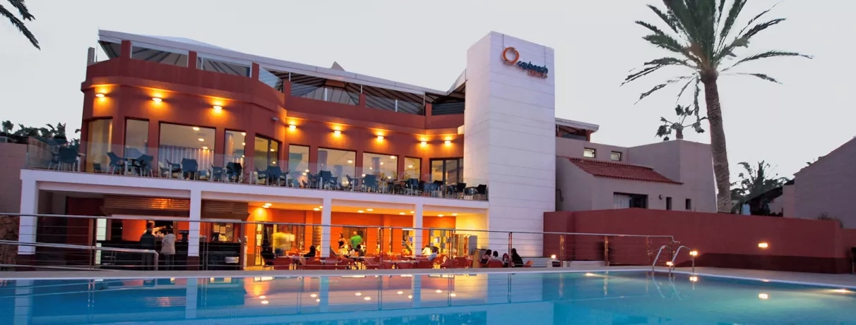 Une vue nocturne élégante où les éclairages chaleureux de l'hôtel se reflètent dans la piscine.