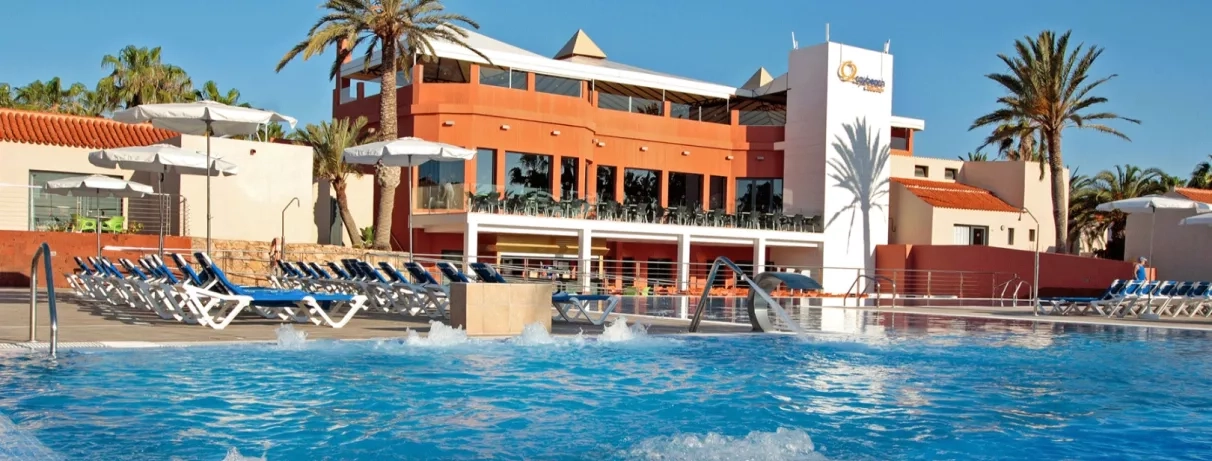 L'établissement se dévoile sous un grand ciel bleu, avec sa façade et sa piscine.