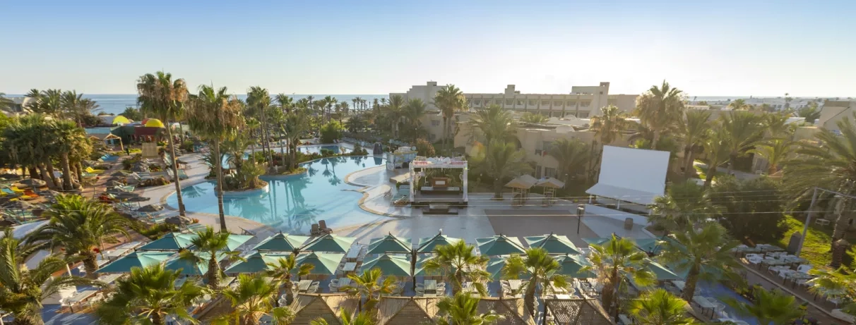 Vue panoramique des infrastructures, piscines et jardins luxuriants de l'hôtel Welcome Meridiana à Djerba en bord de mer.