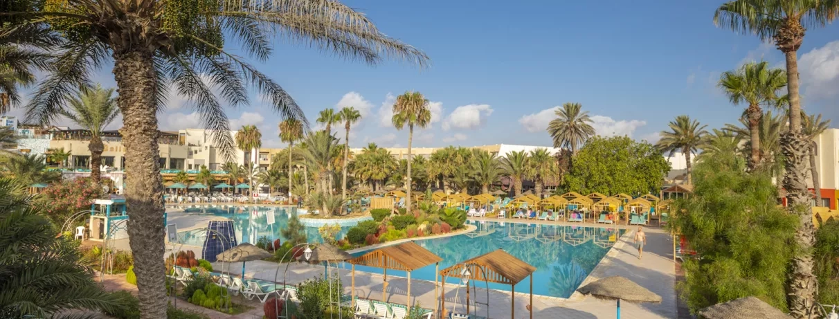 Grande piscine azur entourée de palmiers et paillotes au complexe hôtelier Welcome Meridiana à Djerba, Tunisie.