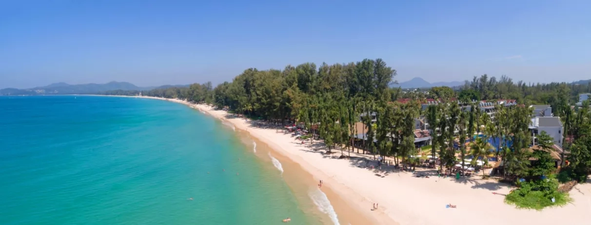 Une vue aérienne d'une plage de sable blanc avec de l'eau turquoise, bordée par une forêt tropicale.