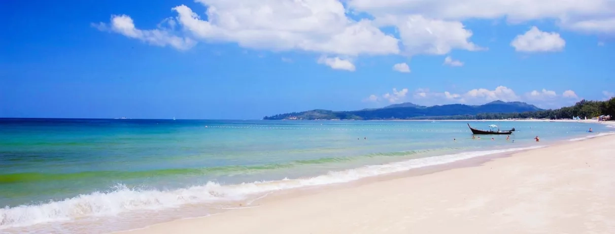 Plage de sable fin et d'eau cristalline sous un ciel bleu.