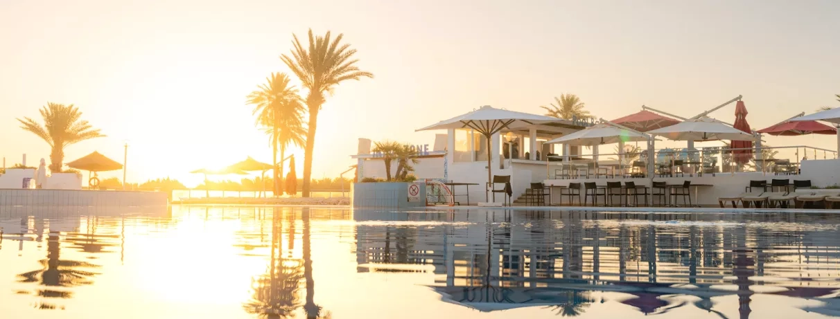 Piscine extérieure au coucher du soleil avec palmiers et bar au One Resort Aqua Park Monastir.