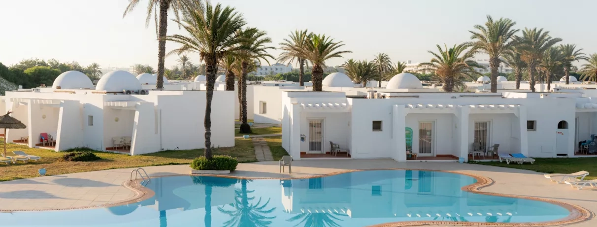 Bungalows blancs typiques et piscine azur entourés de jardins au One Resort Aqua Park à Monastir.