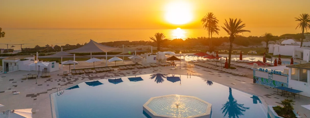 Vue panoramique sur la grande piscine éclairée et la plage au crépuscule à Monastir, Tunisie.