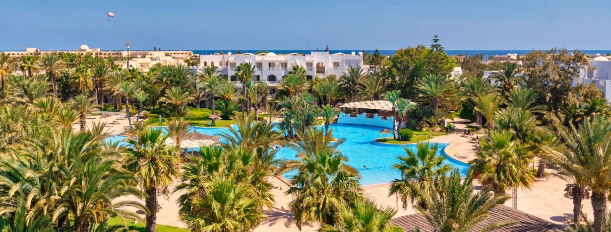 Vue panoramique sur la piscine lagon et les jardins tropicaux du Djerba Resort sous le soleil.