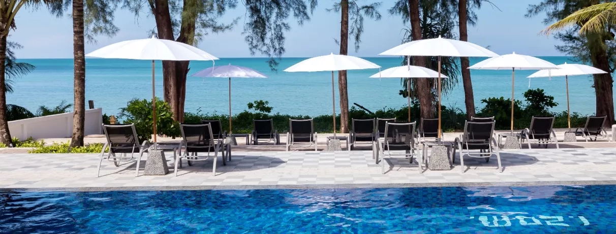 Vue d'une piscine bordée de palmiers avec des parasols blancs, des transats.