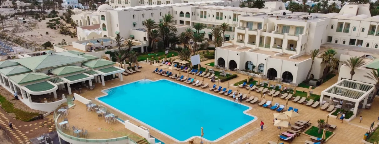 Grande piscine extérieure bleue et terrasse ensoleillée avec transats à l'hôtel Ulysse Djerba en bord de mer.