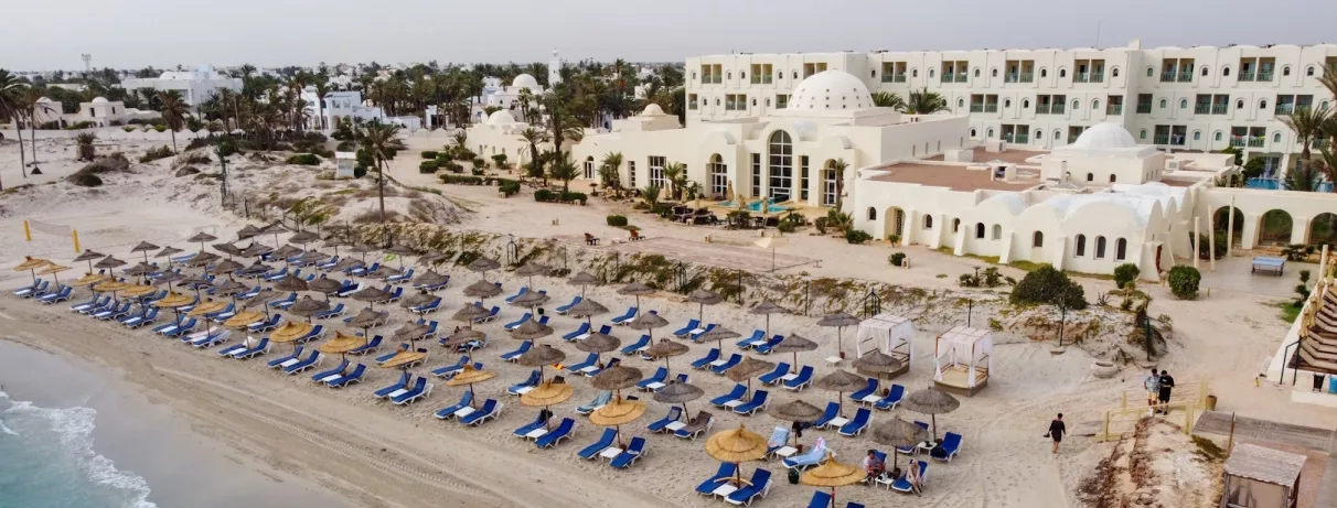 Vue aérienne de la plage privée de l'hôtel Ulysse Djerba avec parasols en paille et sable fin.
