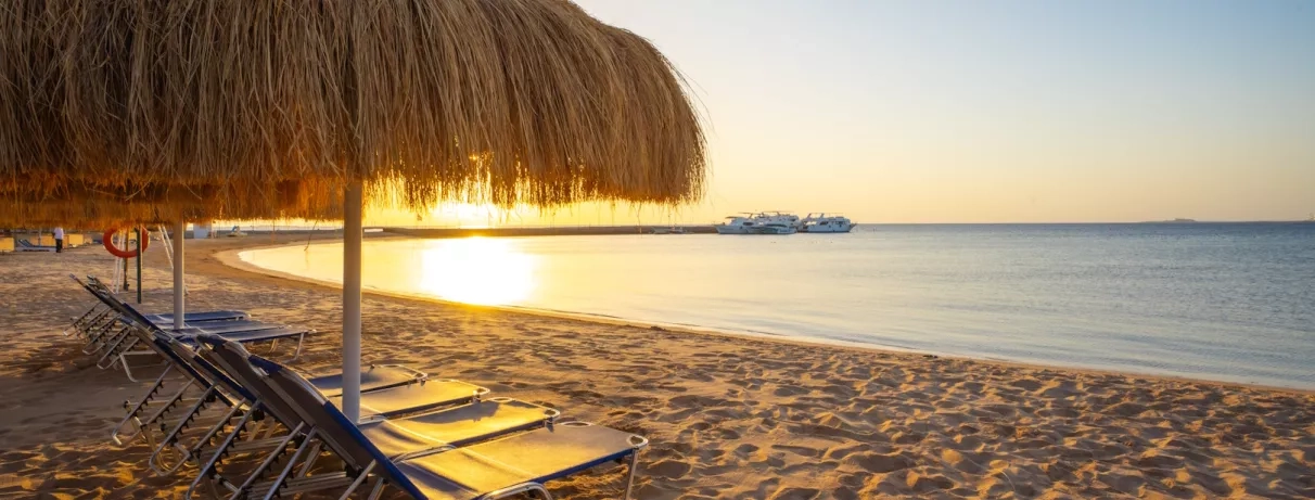 parasols, transats, au bord de la mer, sable fin, yacht sur le quai, coucher de soleil