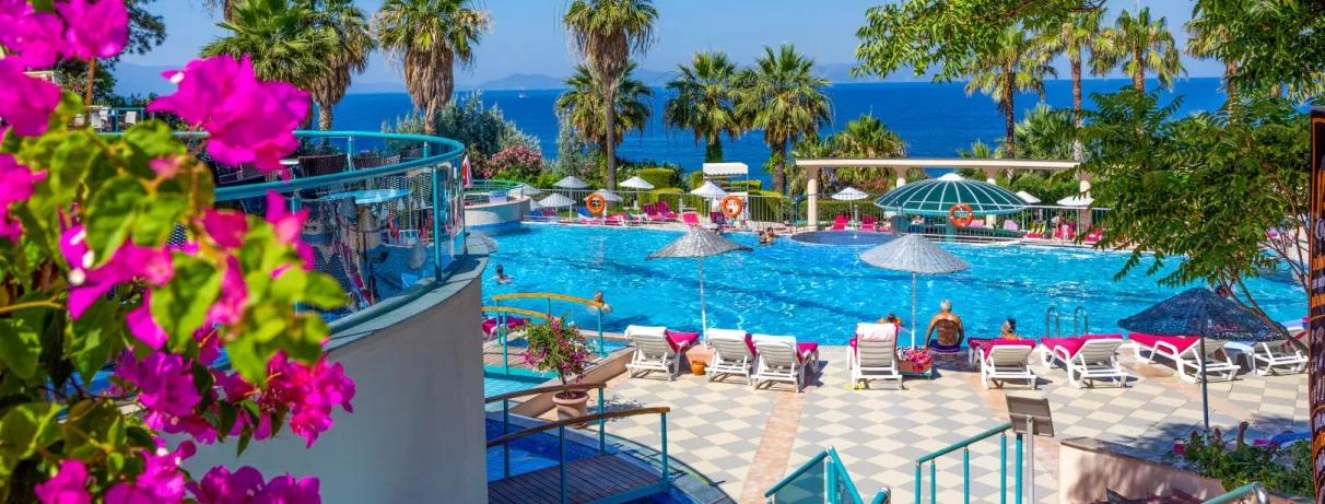 Une piscine animée sous un ciel bleu, entourée de parasols et de palmiers.