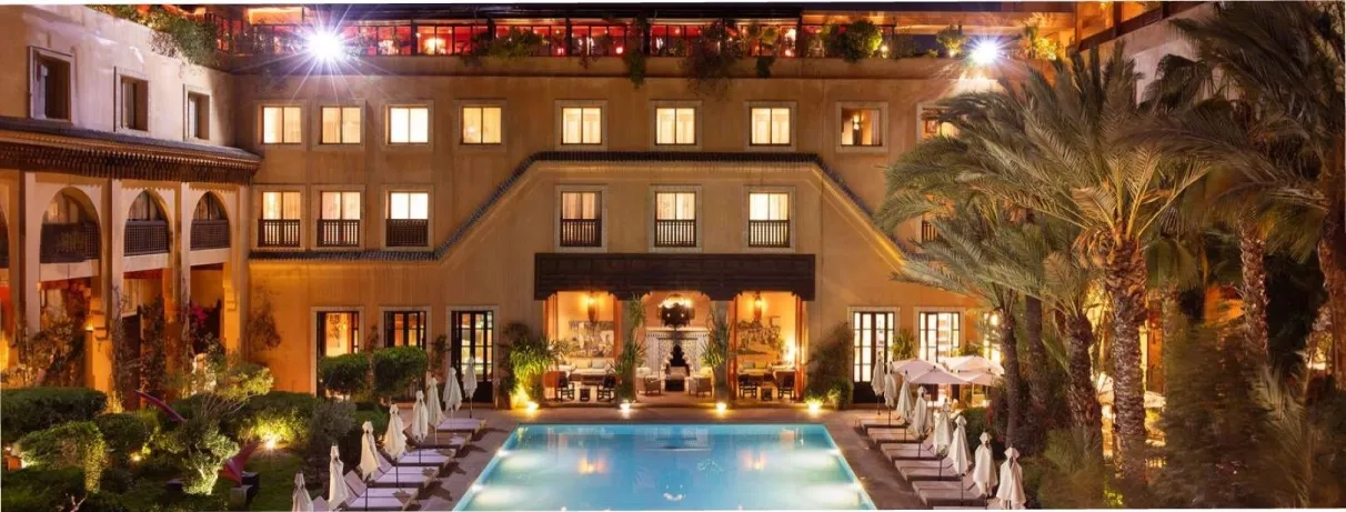 Vue Générale sur la piscine extérieure avec des transats au bord de la piscine et un salon marocain à toit couvert  le soir