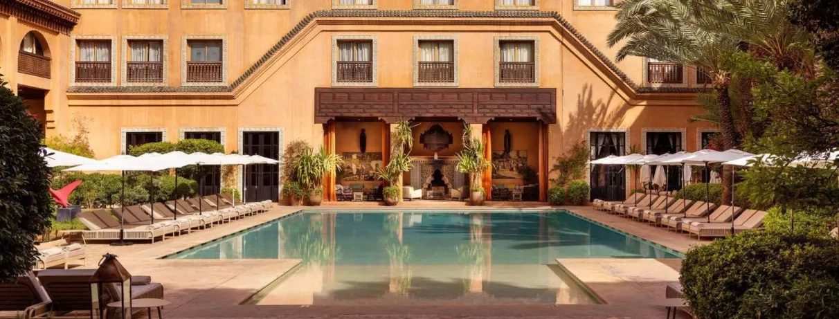 Vue Générale sur la piscine extérieure avec des transats au bord de la piscine et un salon marocain à toit couvert  