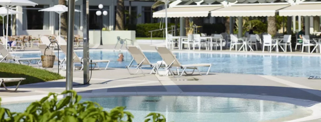 piscine avec transats autour, terrasse avec des auvents beiges, et chaises et tables