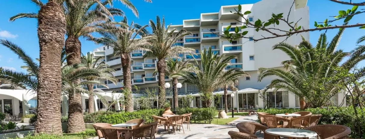 palmiers, tables et chaises pour se poser, façade de l'hôtel avec balcons, plein de plantes