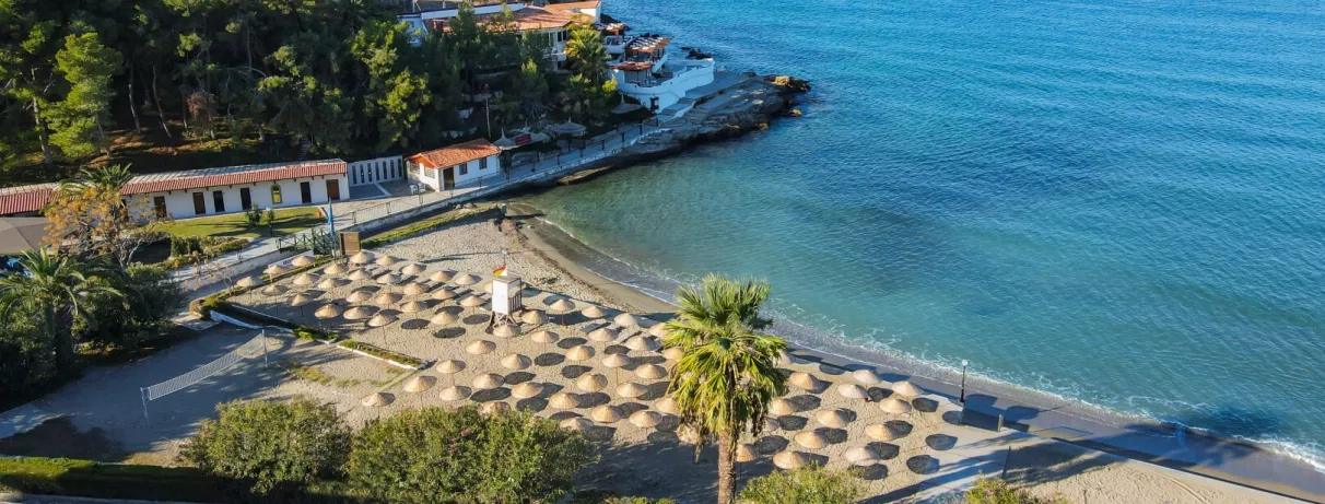 Une vue plongeante sur une plage avec de nombreux parasols alignés au bord d'une eau turquoise.