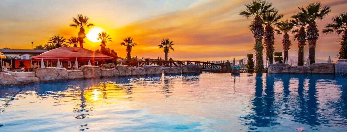 Un coucher de soleil se reflétant sur les eaux calmes de la piscine bordée de palmiers.