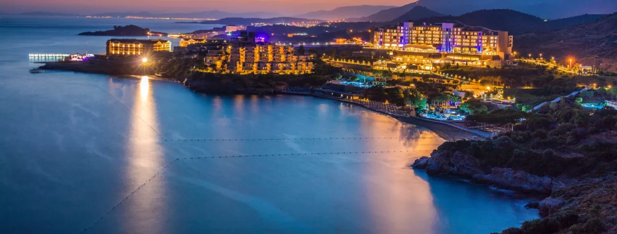 Une vue nocturne du complexe illuminé se reflétant dans les eaux calmes de la baie.