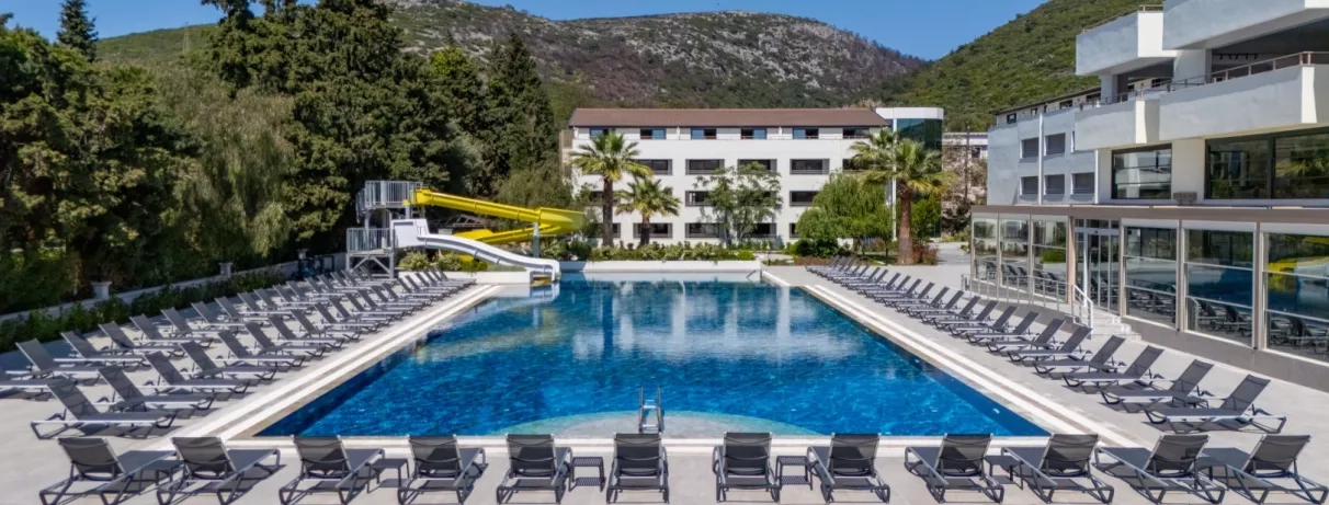 Une vue d'une grande piscine entourée de nombreux transats, avec les bâtiments de l'hôtel.