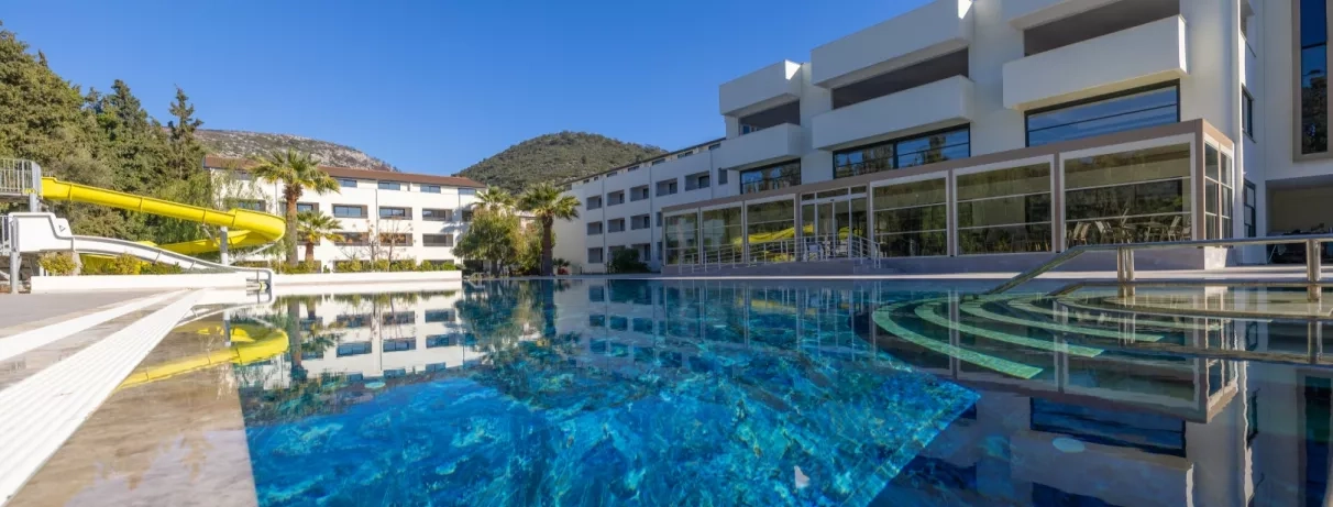 Une vue en perspective montrant les reflets dans la piscine et la terrasse couverte du bâtiment principal sur la droite.