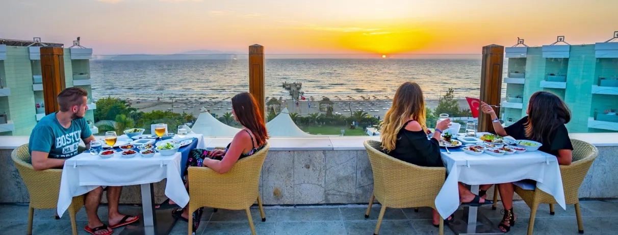 Des clients profitant d'un dîner en terrasse face à un coucher de soleil sur la mer.