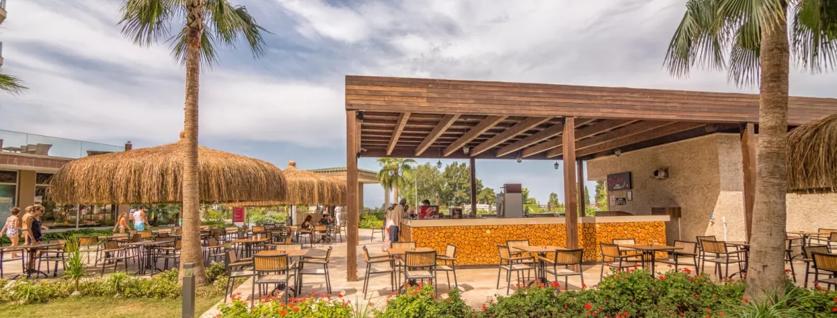 Un bar extérieur moderne avec des tabourets, entouré de palmiers autour.