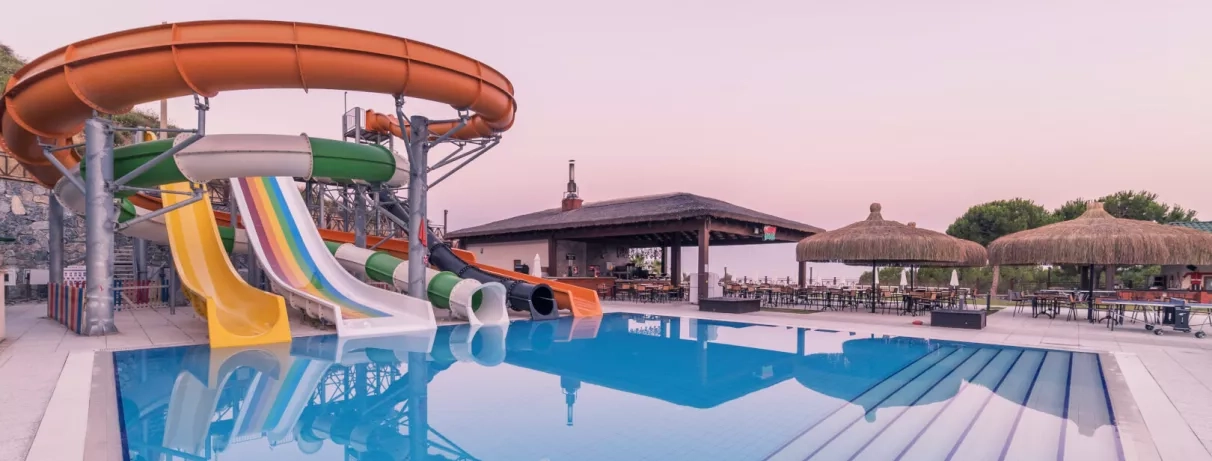 Un parc aquatique animé avec des toboggans et un bar de piscine sous un ciel rosé.