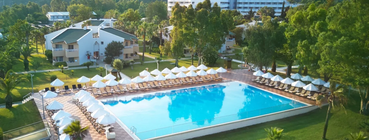 Un bassin bleu niché au cœur d'un jardin méditerranéen avec des bâtiments en arrière-plan.
