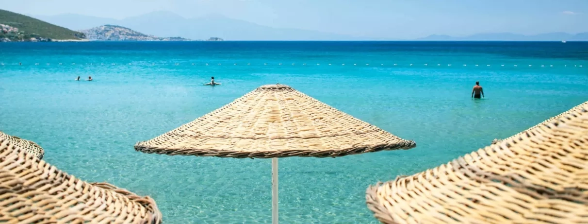 Des parasols en pailles, sur la plage face à une mer calme et turquoise.
