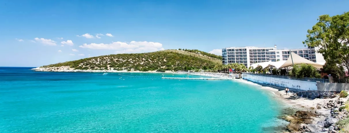 Un large panorama d'une baie protégée aux eaux cristallines, longeant une plage de sable fin.