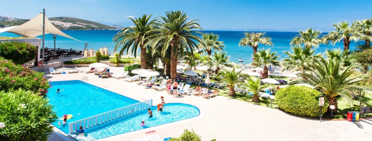 Une vue plongeante sur la piscine, bordée de palmiers avec la mer en arrière-plan.