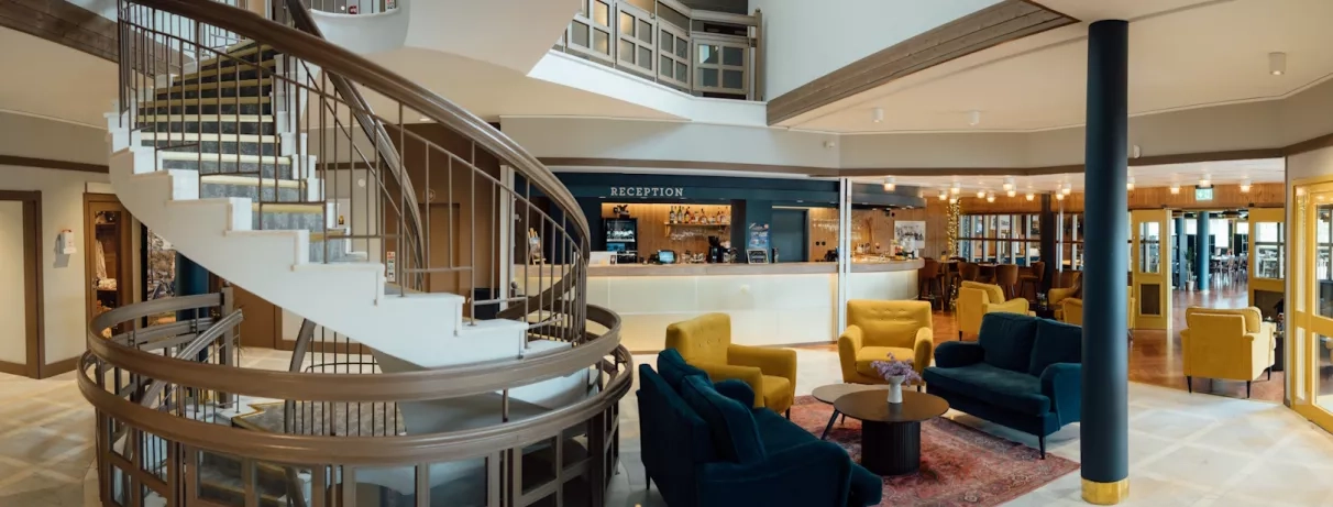 réception avec escaliers, fauteuils et tables, comptoir d'accueil
