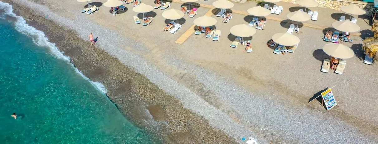 Une vue sur la plage, l’eau turquoise et les parasols en paille.