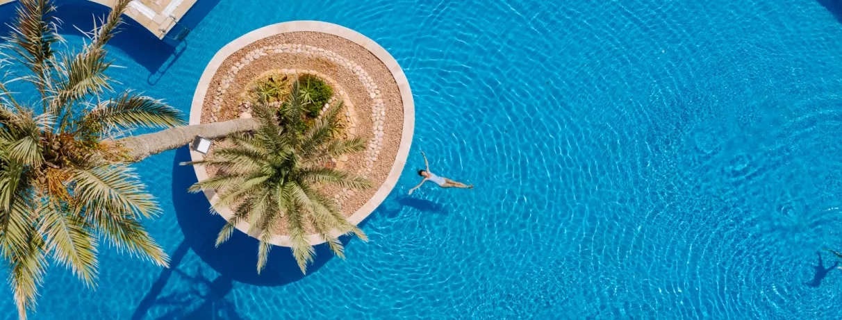 Femme nageant dans l'eau bleue d'une piscine circulaire avec palmier central au Djerba Golf.