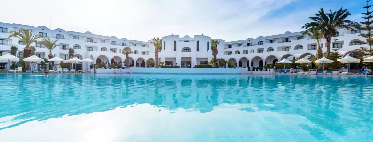 Piscine lagon et façade de l'hôtel Palm Azur sous un ciel bleu clair en Tunisie.