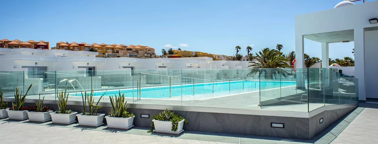 Une piscine aux eaux turquoise est entourée de rangées de plantes, sous un ciel bleu.