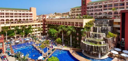 Un complexe hôtelier moderne avec plusieurs piscines entourées de palmiers et de chaises longues.
