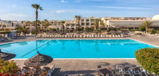 Grande piscine extérieure entourée de palmiers et de transats sous le soleil de Djerba, en Tunisie.