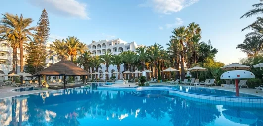 Grande piscine bleue entourée de palmiers et parasols au complexe hôtelier Marhaba Beach à Monastir, Tunisie.