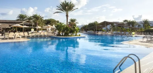 Grande piscine extérieure ensoleillée avec structures en bois et végétation tropicale au complexe Seabel Rym Beach.