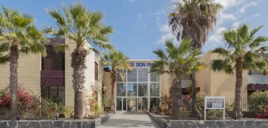 Une allée centrale bordée de palmiers et de bâtiments modernes sous un ciel bleu dégagé.